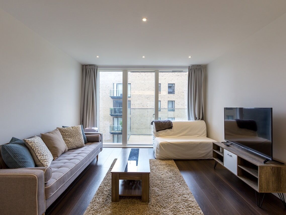 A modern living room with a sofa, a coffee table, a TV, and a large window with curtains.