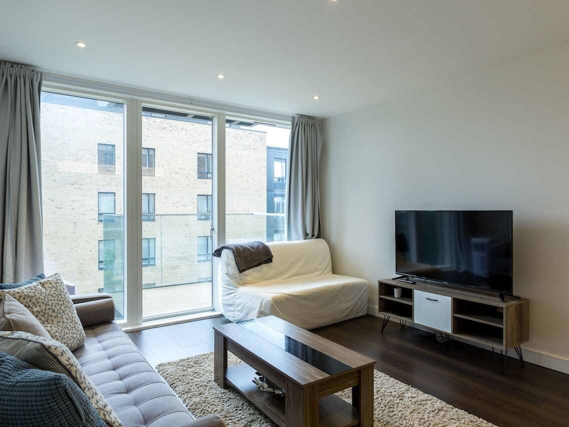 Un salon moderne avec un canapé, une table basse, un téléviseur et de grandes fenêtres donnant sur un immeuble.
