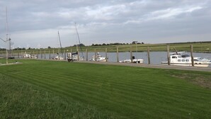A marina with boats docked, a grassy field, and wind turbines in the background. - Renovated vacation home "Alter Schwede" in Scandinavian style / North Sea (Kaiser-Wilhelm-Koog)