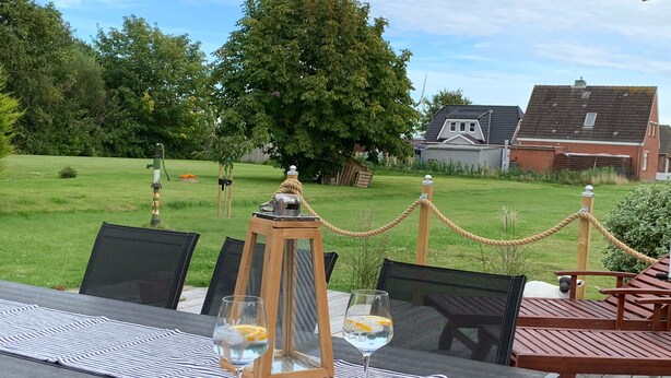 An outdoor dining area with a table set for two, featuring a bowl of chips and two glasses of water. - Renovated vacation home "Alter Schwede" in Scandinavian style / North Sea (Kaiser-Wilhelm-Koog)