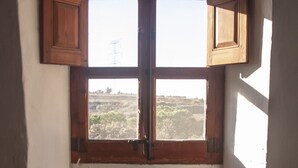 A room with a bay window, two cushioned chairs, a wicker basket with flowers, and a visible landscape outside.