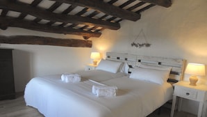 A bedroom with a wooden ceiling, a bed with white linens, two bedside tables with lamps, and a wooden headboard.