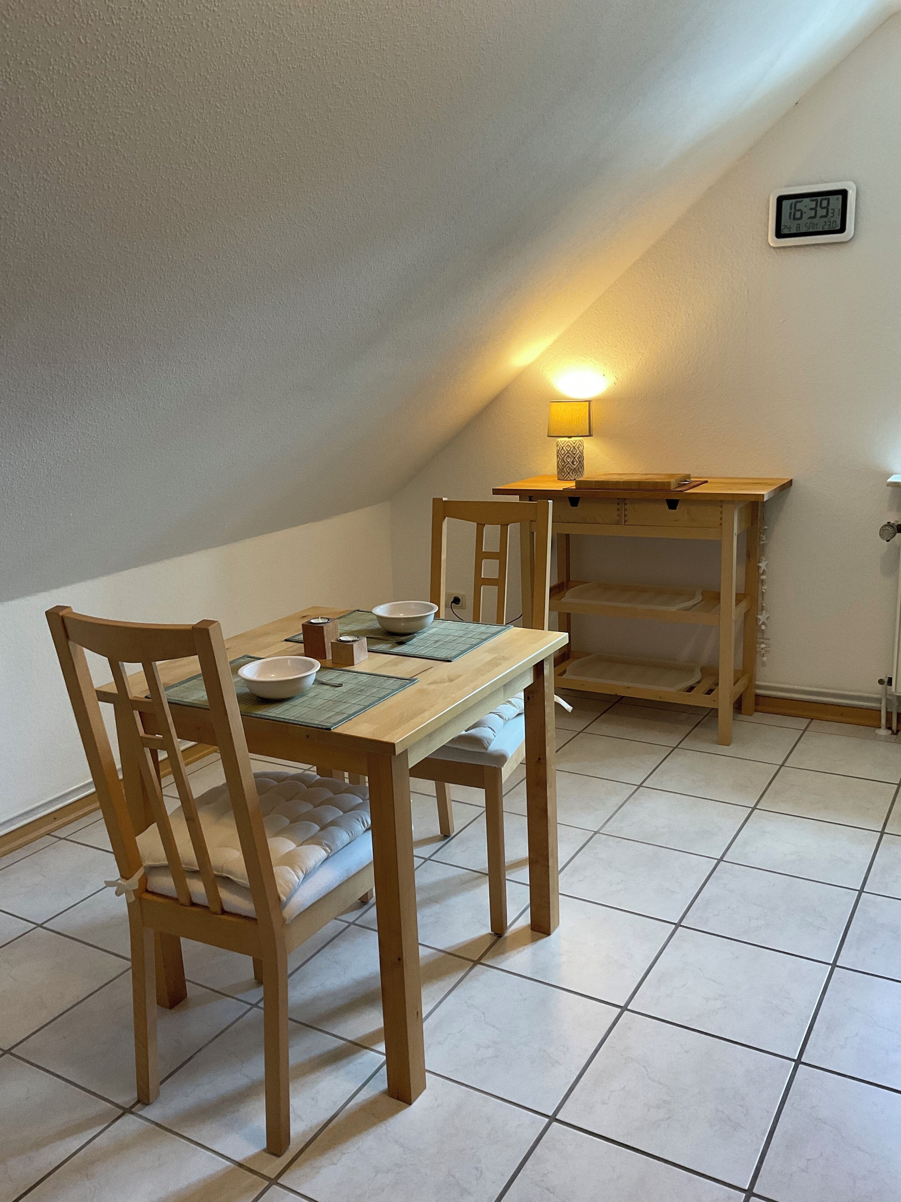 A dining area with a wooden table and chairs, a lamp, and a clock on the wall.