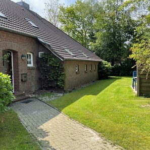 A brick house with a tiled roof, a paved driveway, and a well-maintained lawn. - Idyllically situated. 90m2 apartment for families + travelers up to 5 persons + garden + terrace near the North Sea 🐟 (Marienhafen)