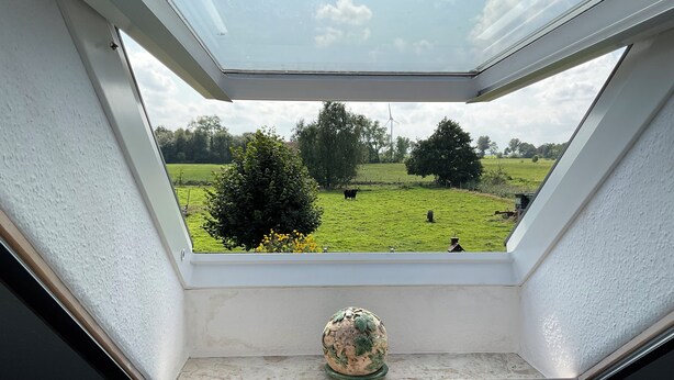 A skylight with a view of a green field, trees, and a wind turbine. - Idyllically situated. 90m2 apartment for families + travelers up to 5 persons + garden + terrace near the North Sea 🐟 (Marienhafen)