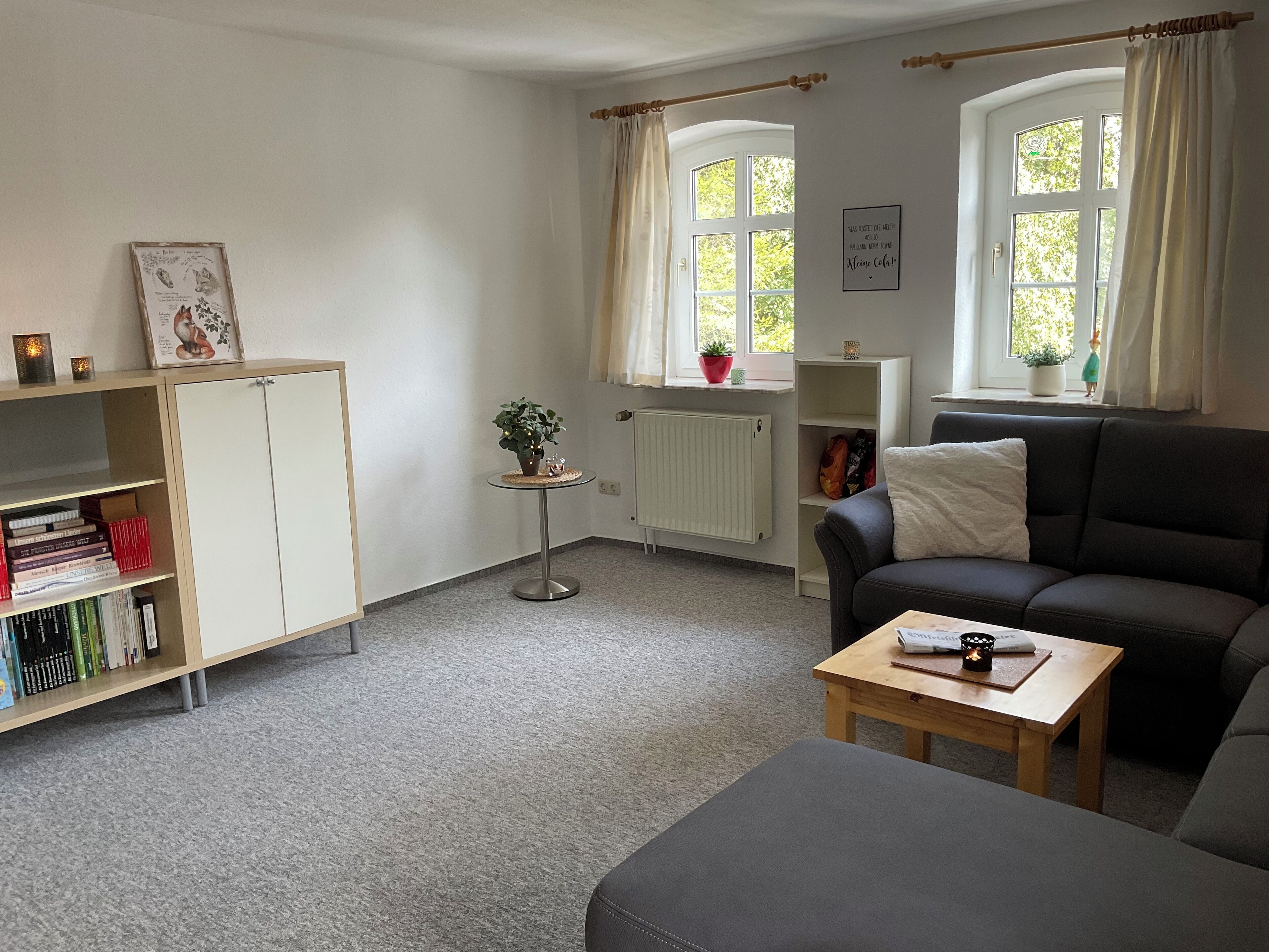 Una sala de estar acogedora con sofá, mesa de centro, estantería, radiador y ventana con cortinas.
