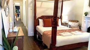 Uma cama com dossel, cabeceira de madeira, mesa de cabeceira com abajur e lareira.