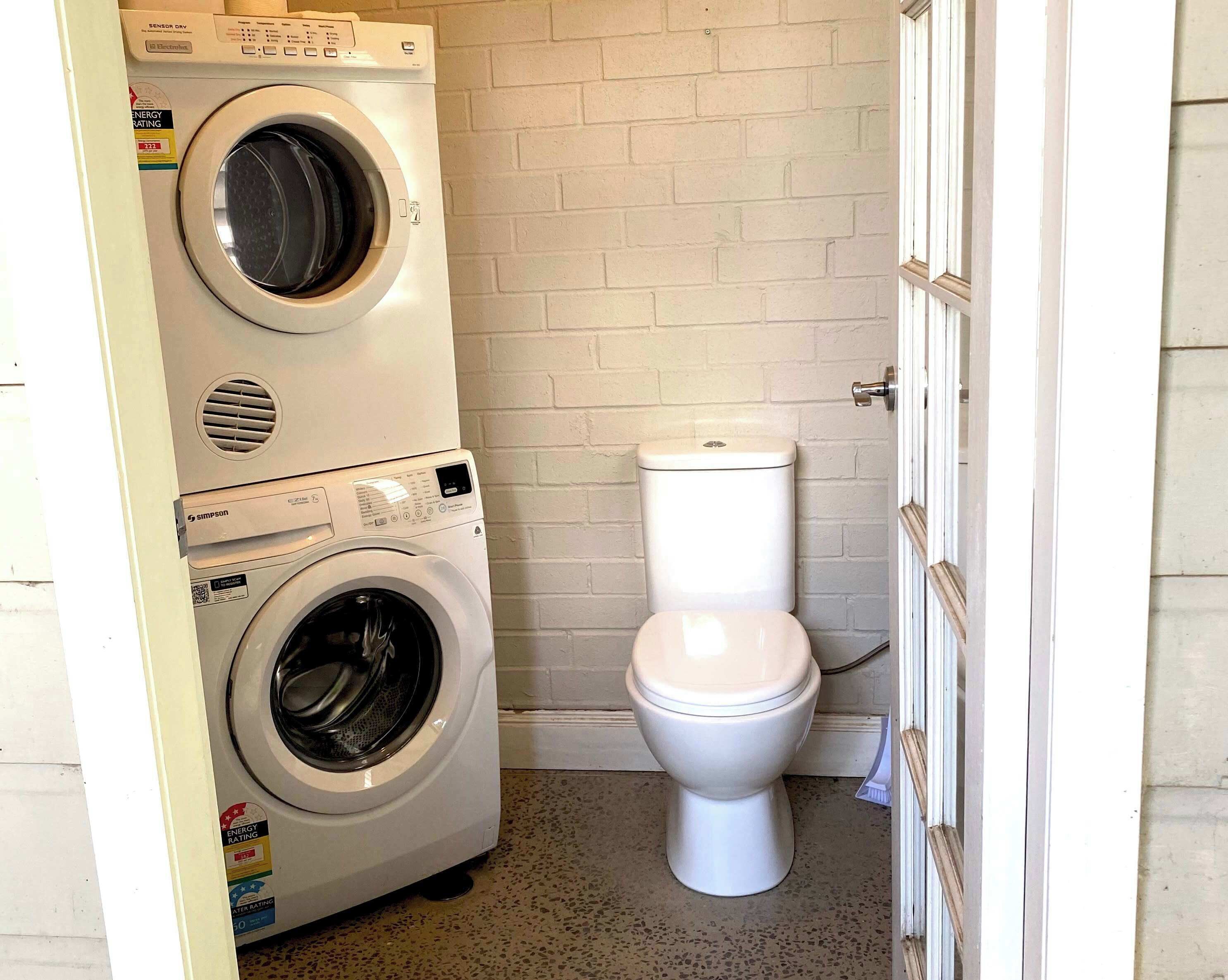 A compact bathroom with a front-loading washer and a toilet.