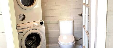 A compact bathroom with a front-loading washer and a toilet.