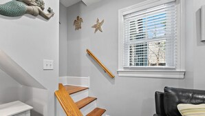 A staircase with wooden steps and a wooden handrail, a white wall with starfish decorations, a window with white blinds, and a black leather sofa with a striped cushion. - *3rd to Beach*Beautiful*Clean*Victorian, *Across VETERANS Prk*Beach Haven  (beach haven)
