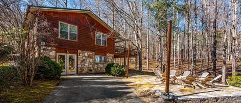 Eine zweistöckige Holzhütte mit Natursteinfundament und einer Veranda, auf der Adirondack-Stühle stehen.