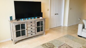 A living room with a flat-screen TV on a wooden cabinet, a door, and a light-colored sofa.