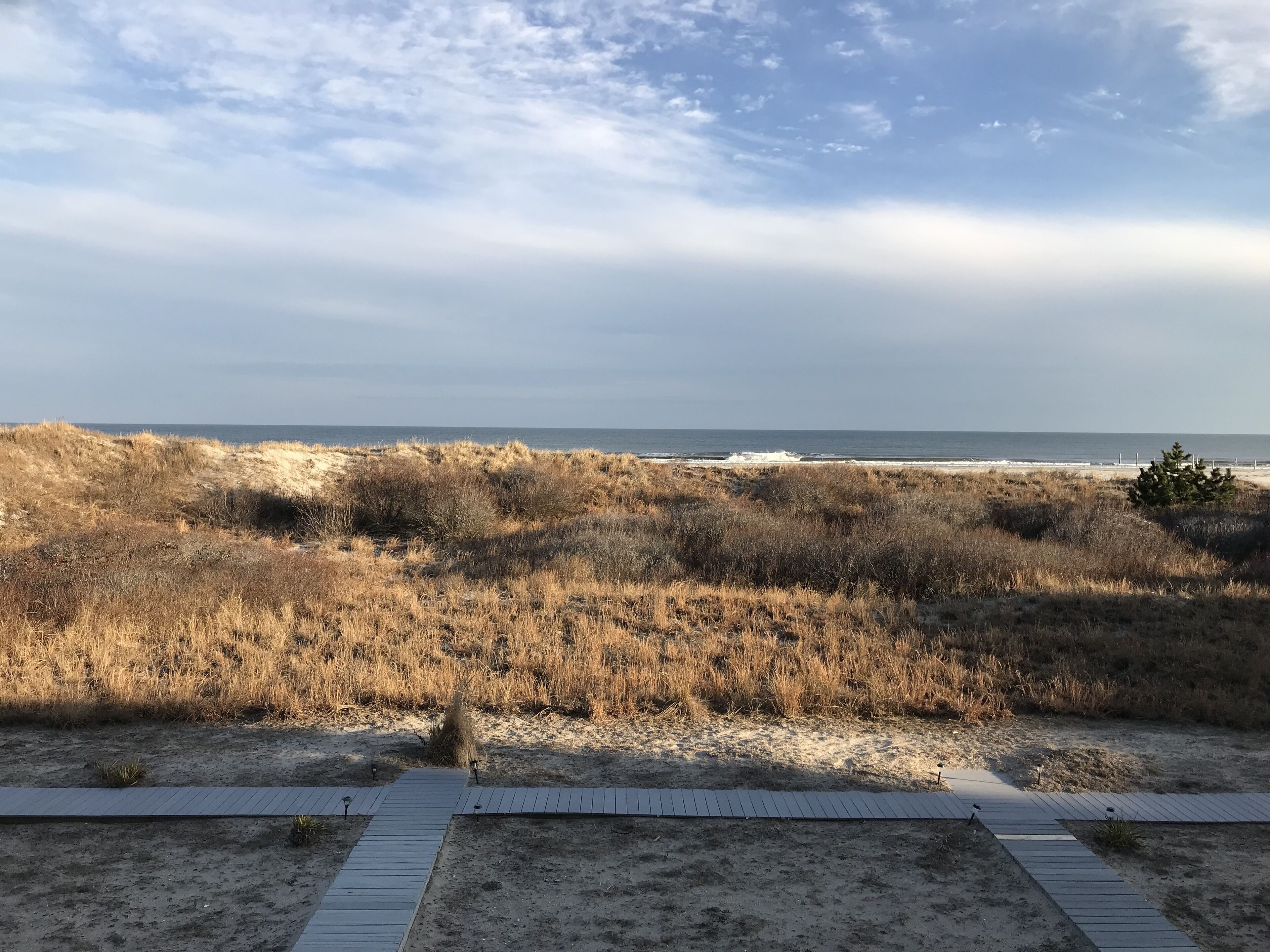 Ein Strand mit einem hölzernen Promenadenweg, der zum Wasser führt, umgeben von trockenem Gras und Dünen.