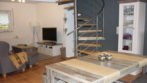 A living room with a sofa, a coffee table, a TV, a staircase, and a cabinet with glassware. - Holiday house in the green north of the Ruhr area (Dinslaken)