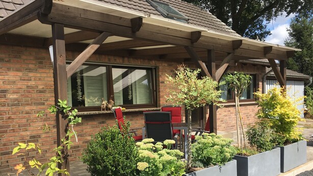 A brick building with a covered patio area, outdoor seating, and various potted plants. - Holiday house in the green north of the Ruhr area (Dinslaken)