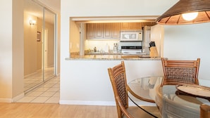 Cocina compacta con microondas, estufa y armarios. Hay una mesa de vidrio con dos sillas.