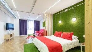 A modern hotel room with a large bed, green artificial grass, a red and white bedspread, a red chair, a wooden nightstand, a television, and a green wall. - Tomate Rooms (Alicante)
