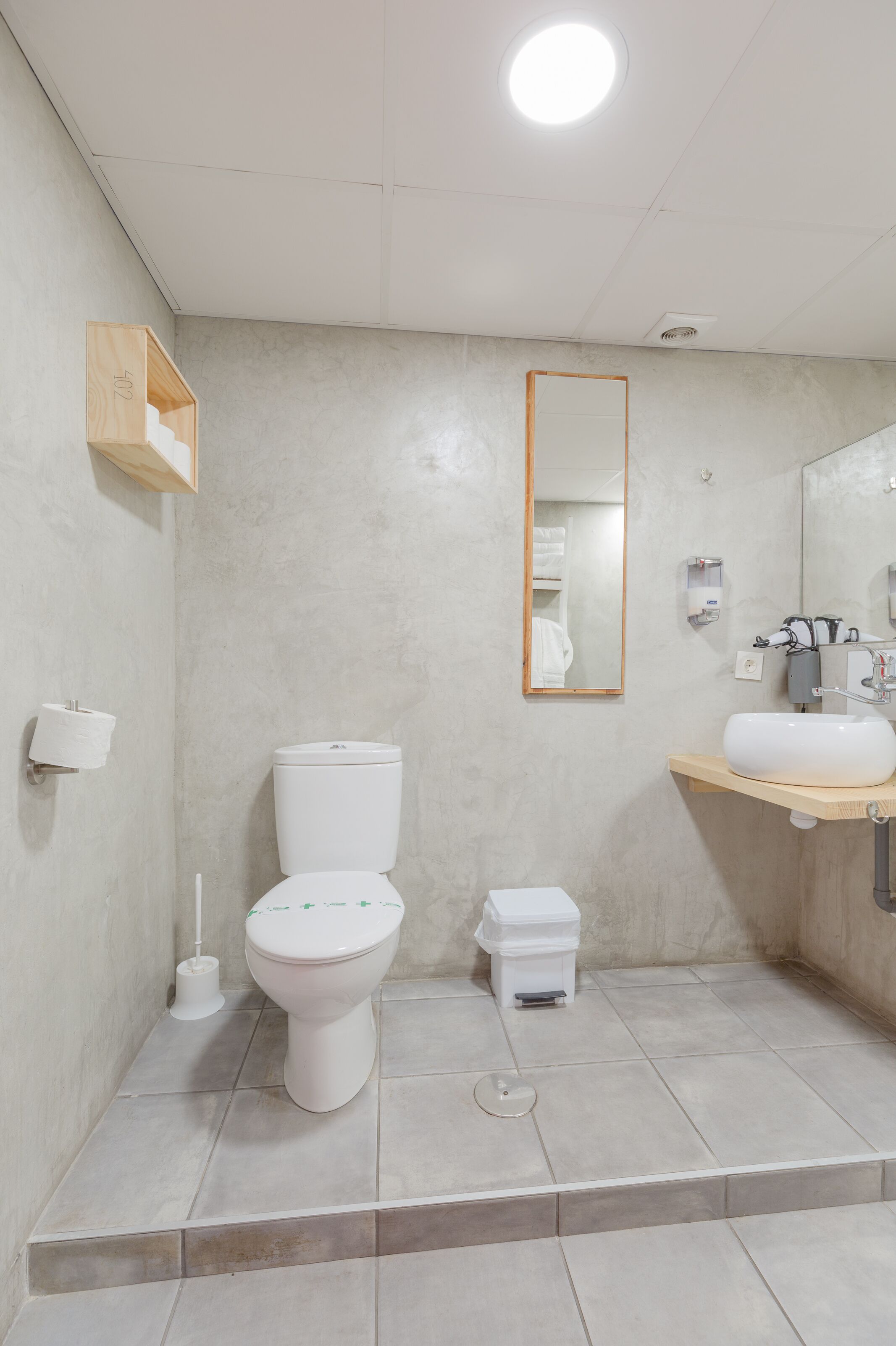 Een moderne badkamer met toilet, wastafel, spiegel en een kleine prullenbak.