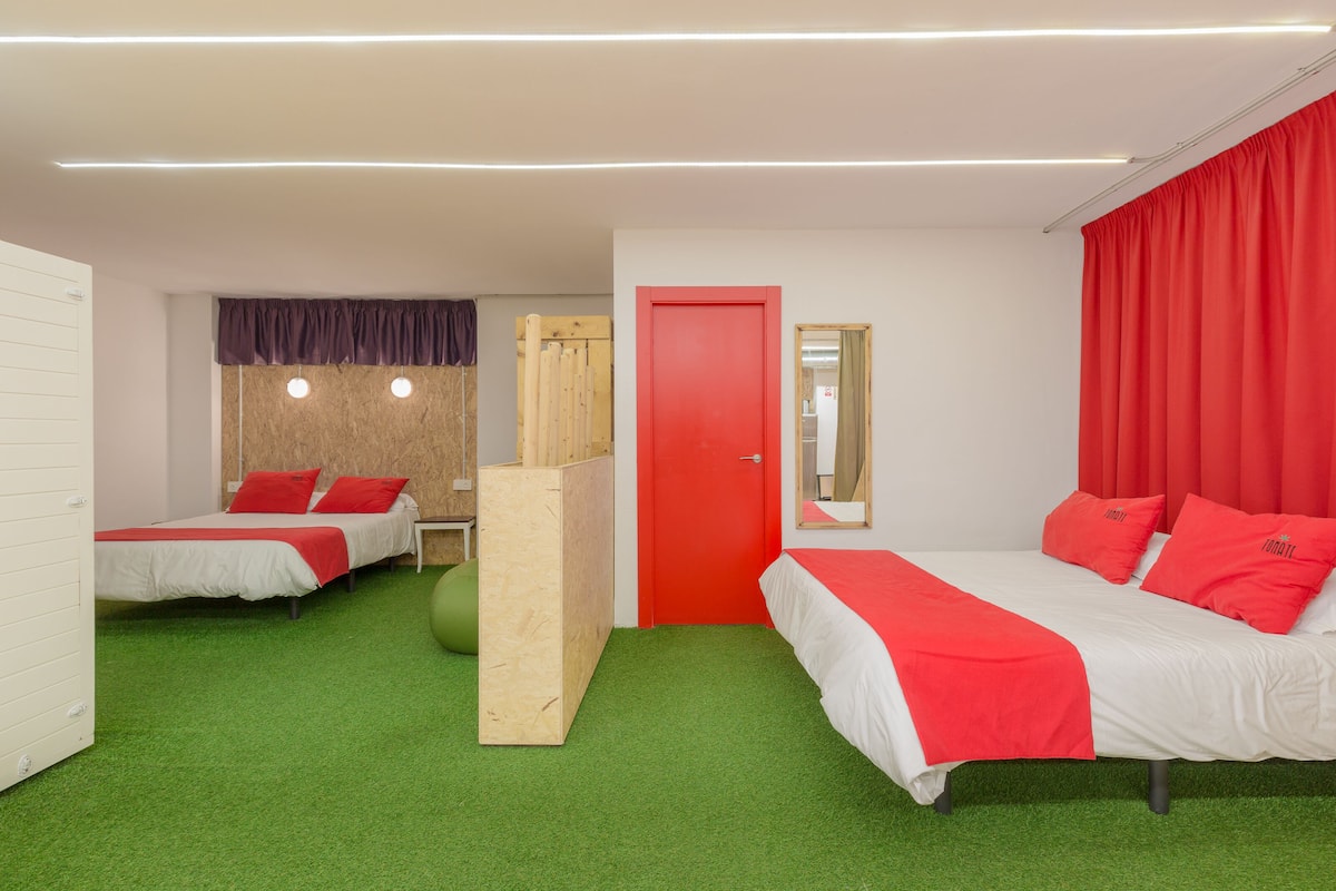 A hotel room with two beds, green carpet, red curtains, and a wooden partition.