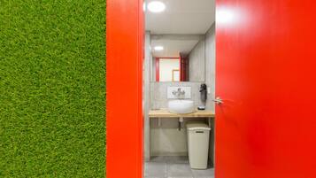 Un baño con pared de césped artificial verde, un lavamanos blanco, un espejo y un cubo de basura.