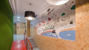 A hallway with a wooden wall mural depicting a map and landmarks, a red metal handrail, and a green wall on one side. - Tomate Rooms (Alicante)