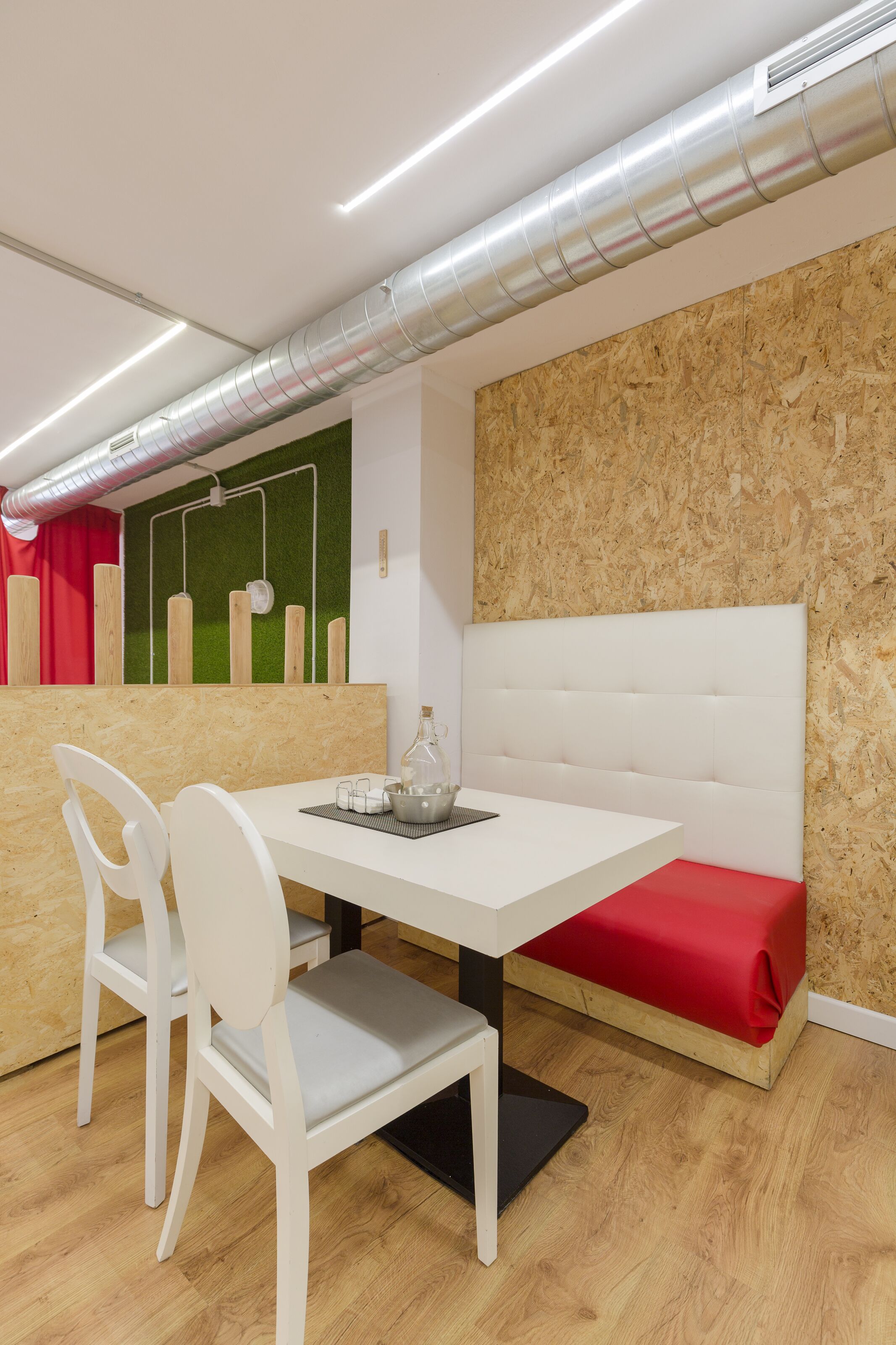 Ein modernes Zimmer mit einem weißen Tisch, zwei weißen Stühlen, einer roten Bank und einer Holzwand mit einem grünen Akzent.