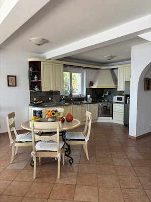 Een keuken met een eethoek, met een ronde tafel met stoelen, een kookplaat en kasten.