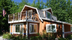 A two-story wooden cabin with a balcony, large windows, and a flag. - Weekly Discount available! 4 Bedroom, 2 Bathroom, Walking Distance To Town (Southwest Harbor)