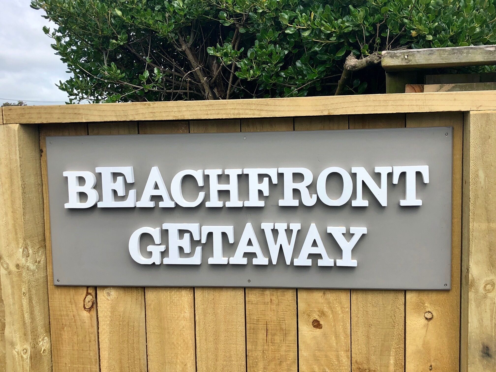 Un letrero que dice 'BEACHFRONT GETAWAY' colgado de una estructura de madera.