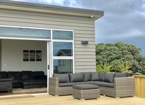 A modern house with a large sliding glass door leading to an outdoor patio area. - Brand New 3 Bedroom Beachfront Getaway.  Beach just across the road. (Otaki Beach)