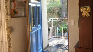 A room with a blue door leading to a balcony with a metal railing and a view of greenery.