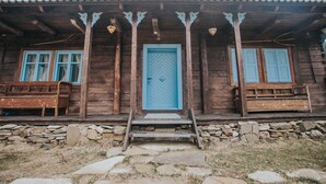 Une maison rustique en bois, avec une porte bleue et deux bancs en bois à l’extérieur.