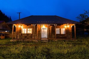 A wooden cabin with a tiled roof, a porch with benches, and a front door. - Gospodaria Lui Nea Ion (Vama Buzaului)
