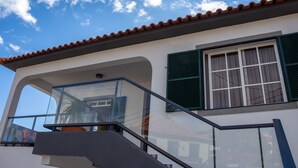 A modern building with a balcony, a staircase, and a window with green shutters.