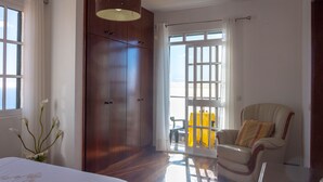 A bedroom with a bed, a wardrobe, a chair, and a view through a glass door.
