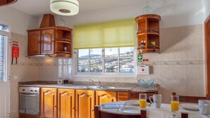 A kitchen with wooden cabinets, a built-in oven, a window with a view of the town, and breakfast items on the table.