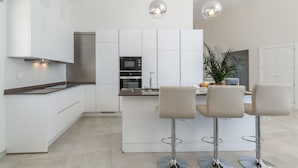 Una cocina moderna con armarios blancos, una isla central con taburetes y luminarias colgantes.