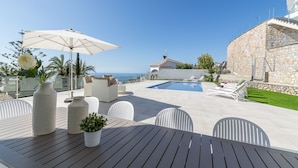 Zona junto a la piscina con un edificio de piedra, mobiliario exterior y vista al mar.