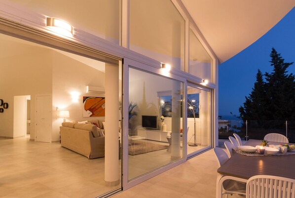 A modern interior with a glass door leading to a dining area, a sofa, and a TV in the background.