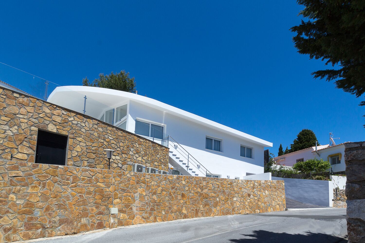 A modern building with a stone facade, a white upper level, and a staircase leading to a flat roof.
