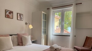 Une chambre à coucher avec un lit, des oreillers, une lampe de chevet, une chaise et une fenêtre donnant sur l’extérieur.