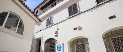 Un bâtiment à la façade blanche, doté de nombreuses fenêtres avec volets, et portant une enseigne indiquant qu’il s’agit d’un commerce ou d’un établissement de services.