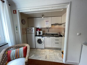 A compact kitchen with white cabinets, a washing machine, a microwave, and a stove.
