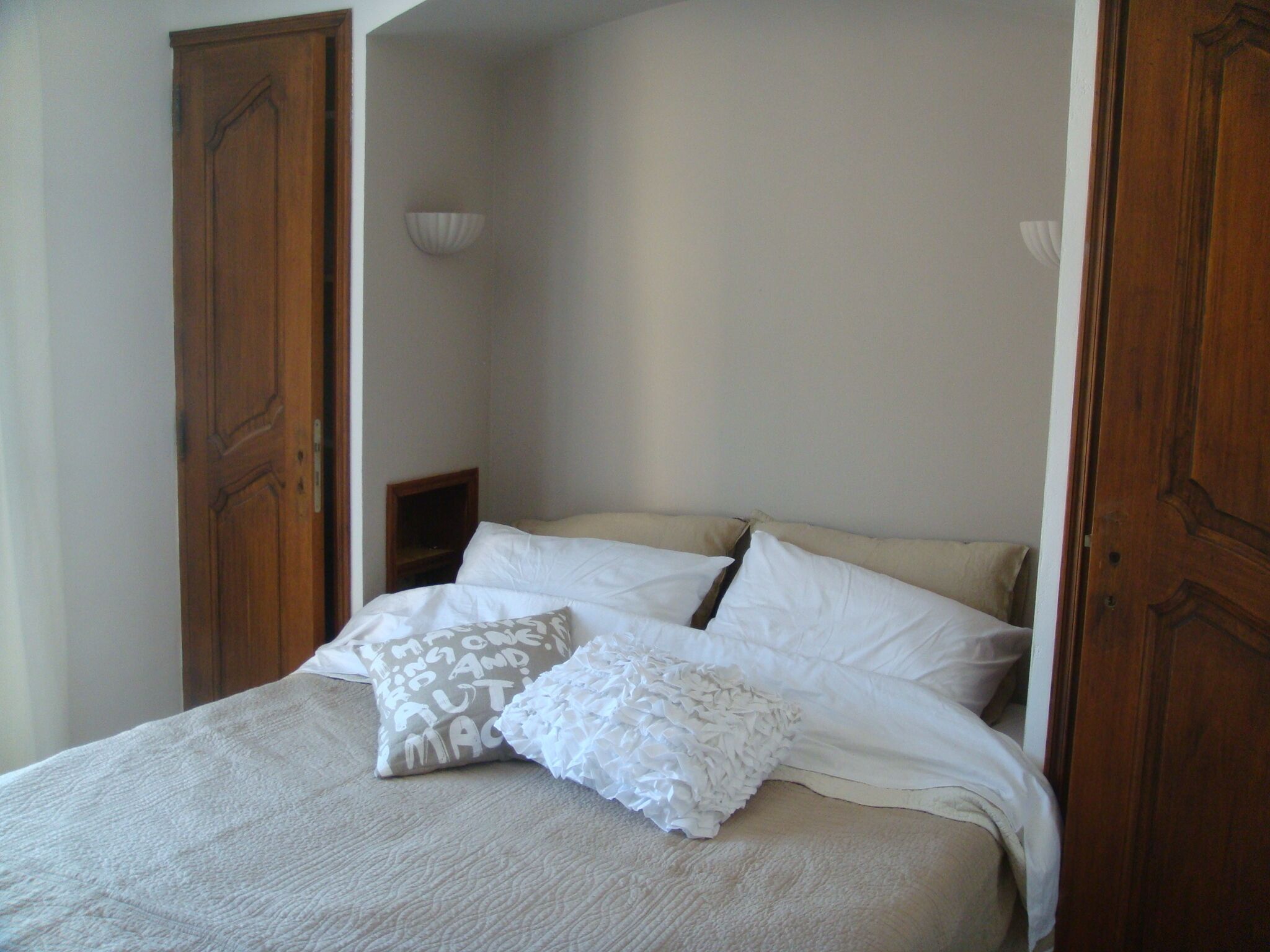 Une chambre à coucher avec un lit, deux oreillers, une table de chevet et une lampe fixée au mur.