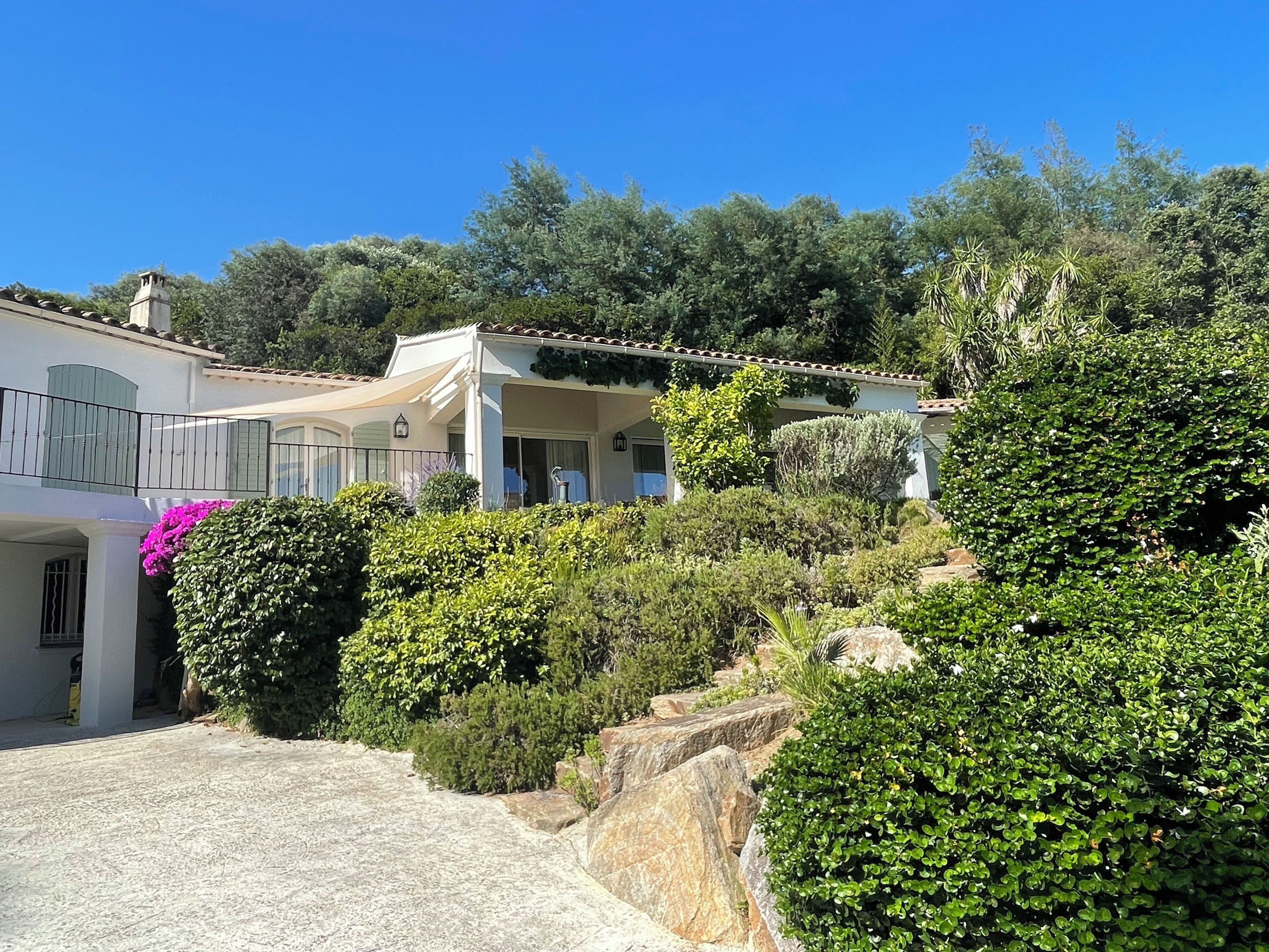 Une maison à deux étages dotée d’un patio couvert, entourée d’une végétation luxuriante et de gros rochers.