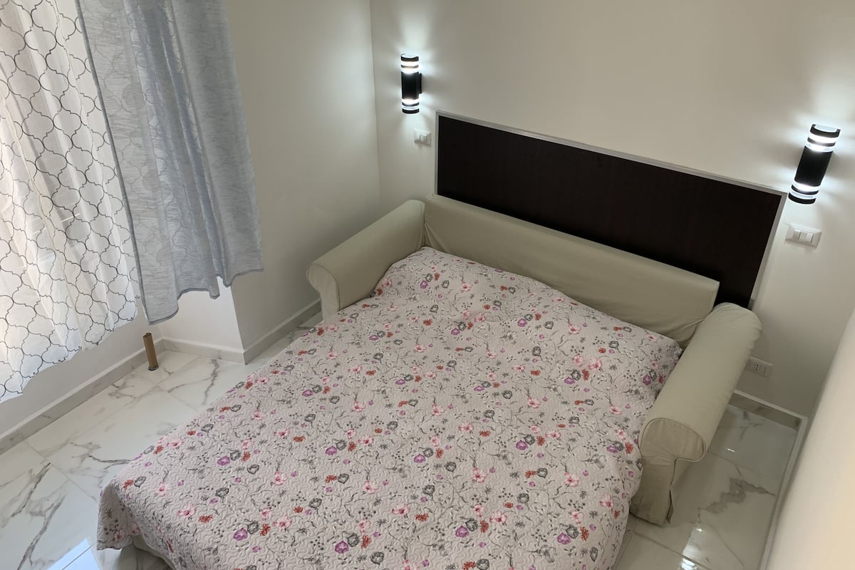 A bedroom with a bed, a headboard, and two wall-mounted lights.