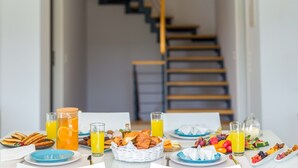 Una tavola imbandita per la colazione con diversi cibi e bevande, un cesto di vimini e una scala sullo sfondo.