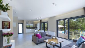 Un'ampia zona giorno con un divano grigio, un tavolino da caffè e una televisione. Una grande finestra offre vista su una piscina e del verde.
