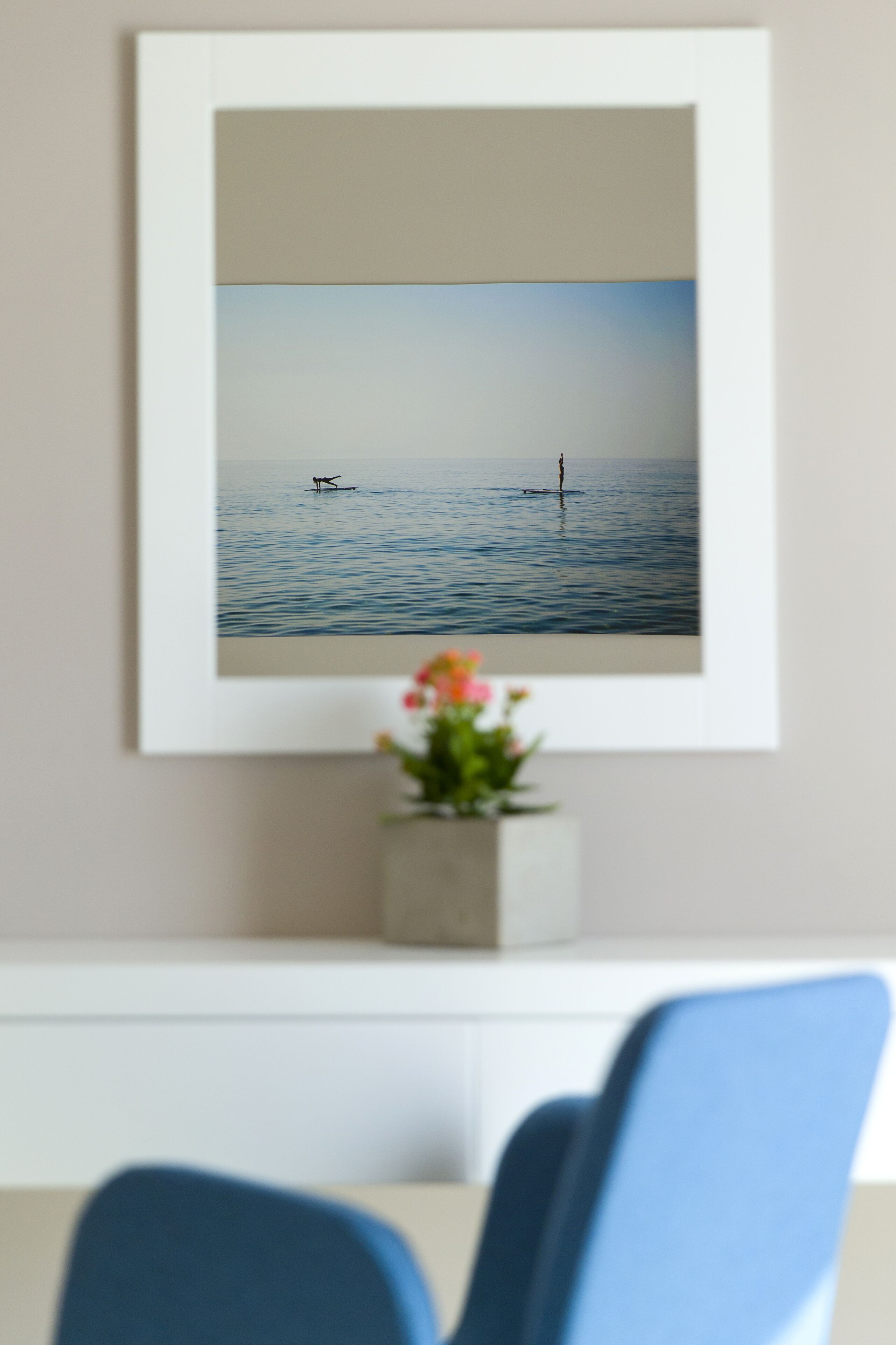 Ein gerahmtes Bild von ruhiger See mit einer Person, die auf einem Bojen steht, an einer Wand über einem Schreibtisch mit Blumentopf.