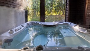 Een jacuzzi met uitzicht op een bos, zichtbaar door een open houten constructie.